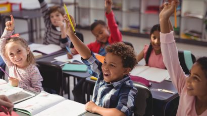 Schoolkids raising their hands in classroom at school